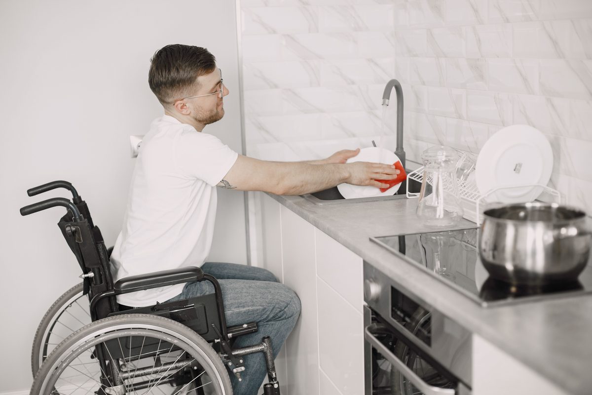 Man using a wheelchair rinsing dishes at the kitchen sink